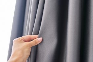 close-up of a woman's hand touching the curtain, gray blackout fabric, light-blocking fabric